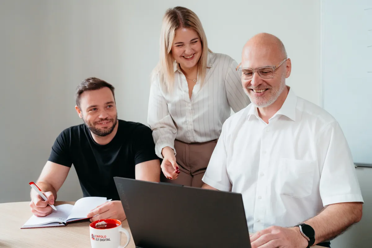 Menschen arbeiten zusammen an einem Laptop im Büro, Junger Mann in schwarzem Hemd lächelt, studiohintergrund, Mitarbeiterfoto, headshot, Businessfoto, Authentische Mitarbeiterfotos